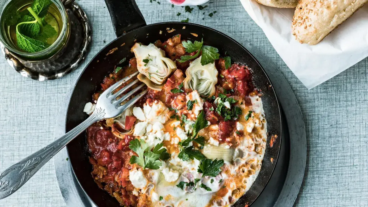 Herzhaftes Menemen ohne Ei mit Artischocken und Feta, garniert mit Petersilie. Dazu frisches Brot und Minztee.
