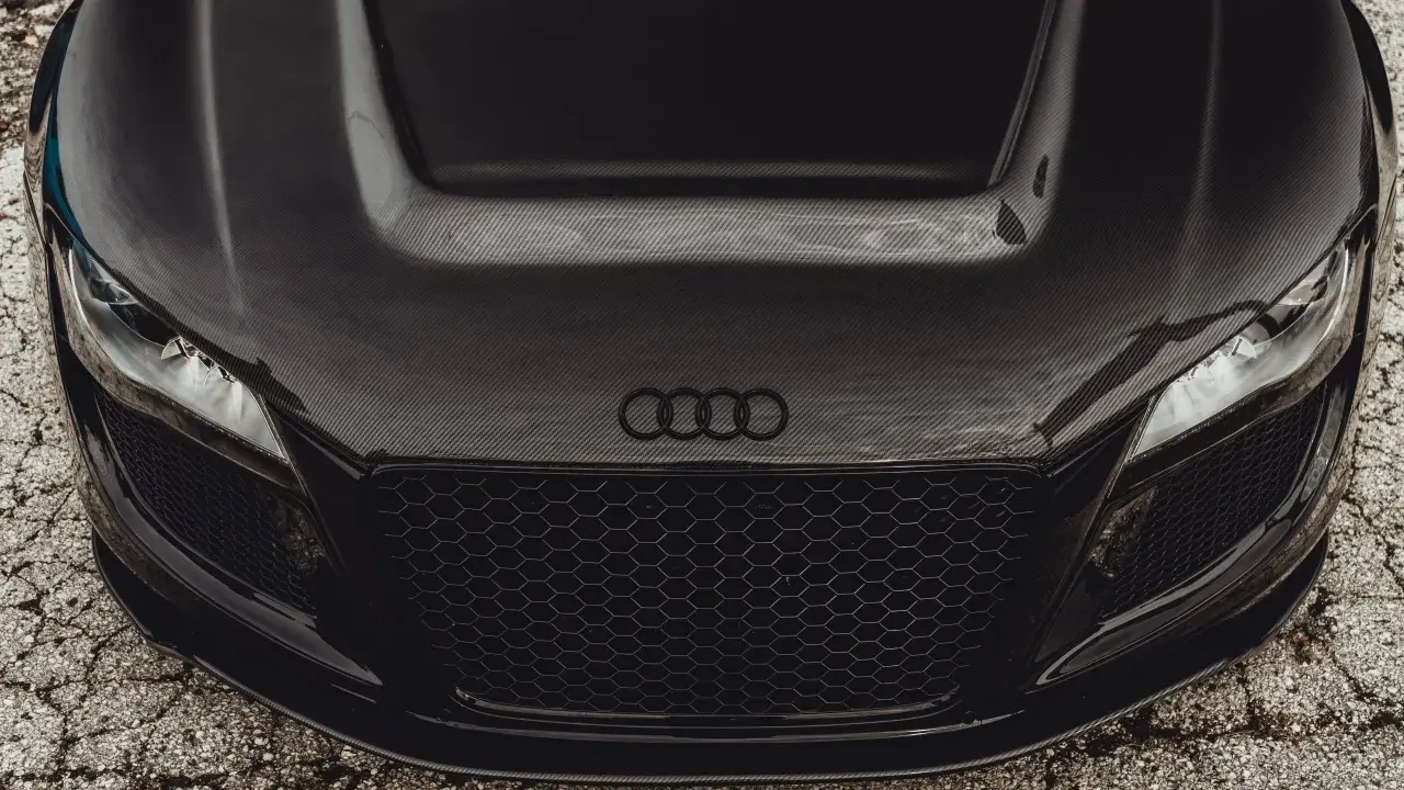 Przód czarnego Audi z maską z włókna węglowego. Widoczne reflektory, atrapa chłodnicy i logo marki.