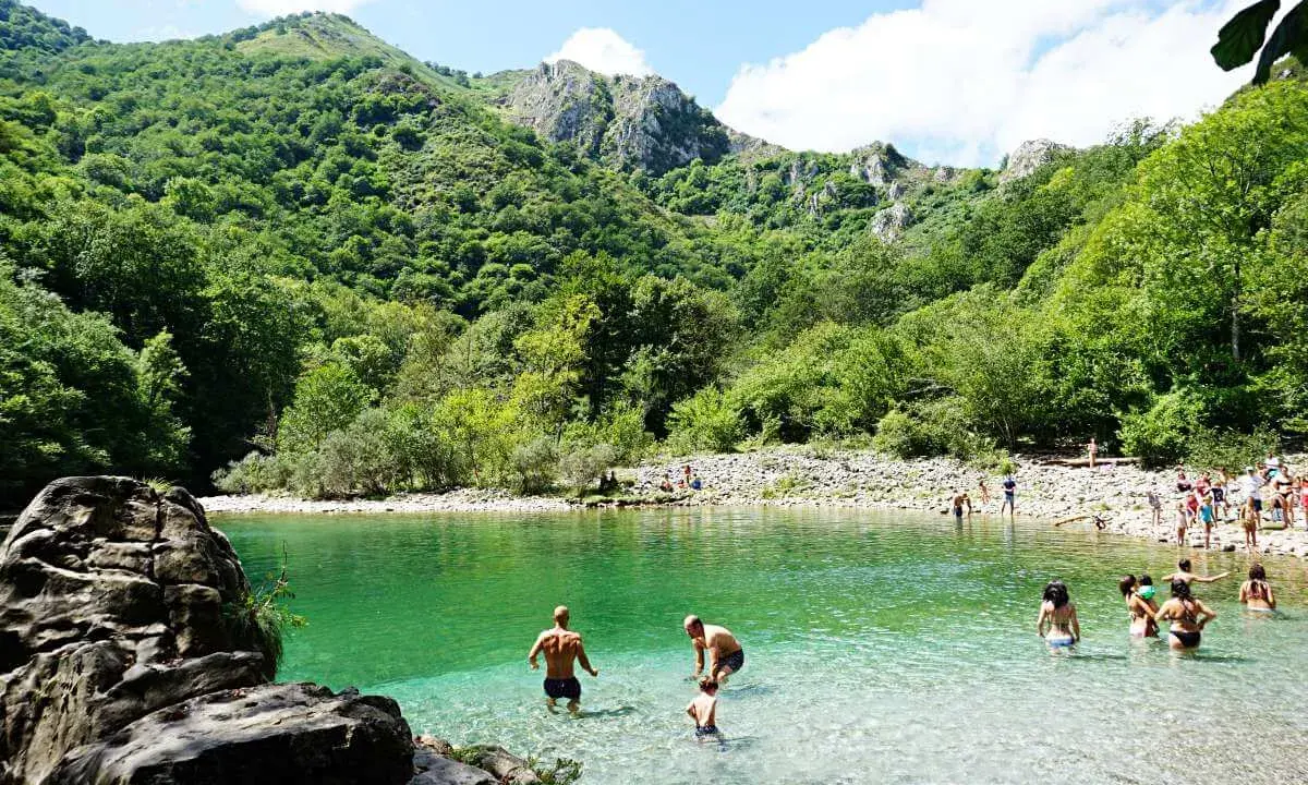 Gente disfrutando del agua cristalina en la olla de San Vicente, rodeada de exuberante vegetación y montañas.