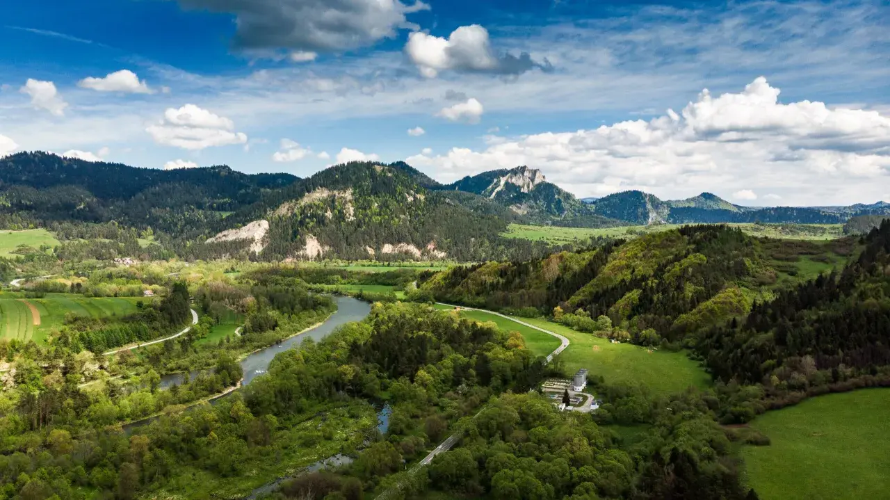 Malownicze **Pieniny** w okolicach **Szczawnicy** z meandrującym Dunajcem, zielonymi łąkami i skalistymi szczytami pod błękitnym niebem.