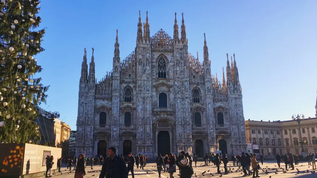Le majestueux Duomo di Milano se dresse sous un ciel bleu, entouré de passants et d'un sapin de Noël décoré.