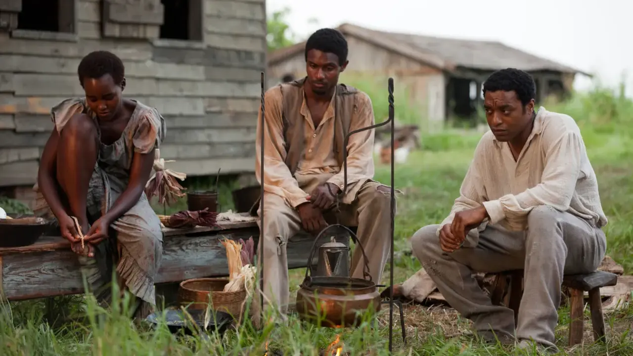 Tre persone sedute all'aperto, in un'ambientazione che ricorda i film biografici sulla schiavitù.