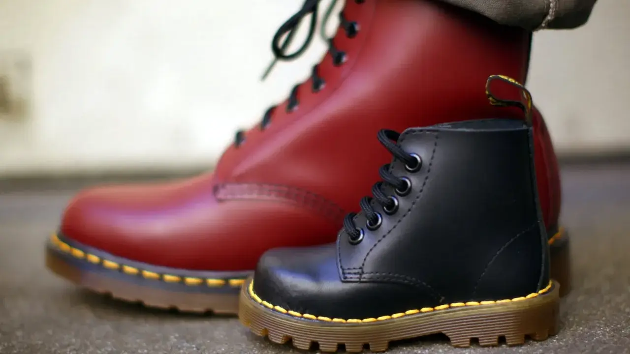 Ein roter und ein schwarzer Dr. Martens Stiefel, die die lange **Dr. Martens Geschichte** von robusten Schuhen für alle Generationen symbolisieren.