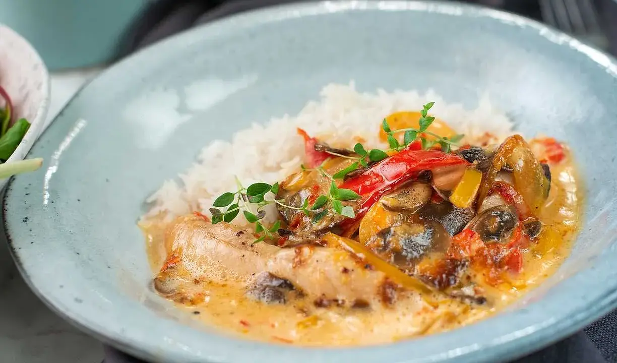 En krämig kyckling- och risrätt med paprika och svamp, garnerad med färska örter. En härlig måltid som ser utsökt ut.