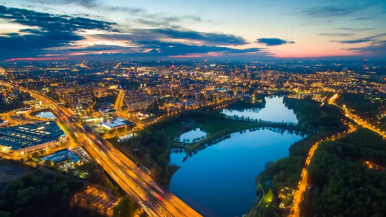 Widok z lotu ptaka na rozświetlone miasto nocą, z autostradą i trzema stawami w tle.