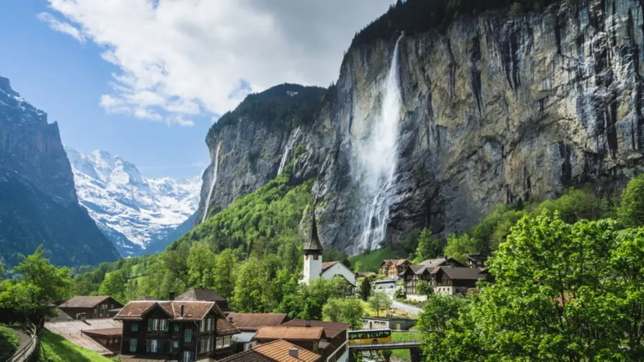 Lauterbrunnen Wasserfall stürzt von einer Felswand, umgeben von einem Dorf und schneebedeckten Bergen.