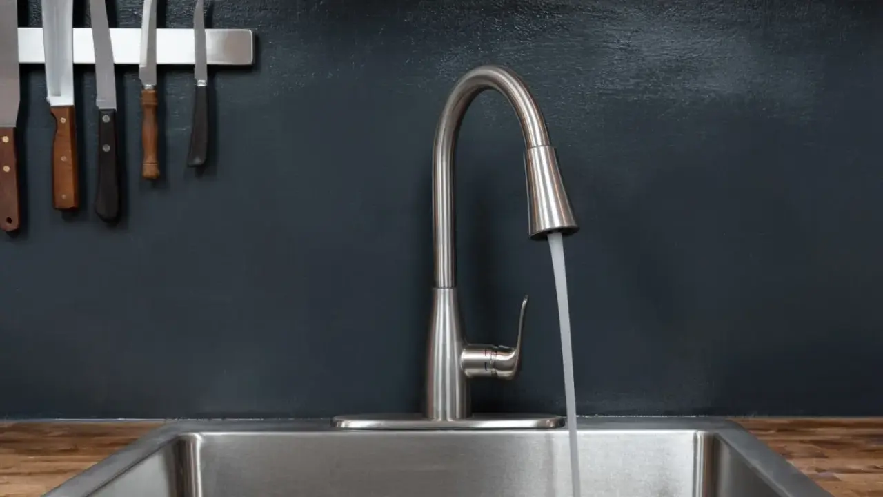 Moderner Küchenwasserhahn für Untertischboiler, der Wasser in ein Spülbecken laufen lässt. Messer hängen an der Wand.