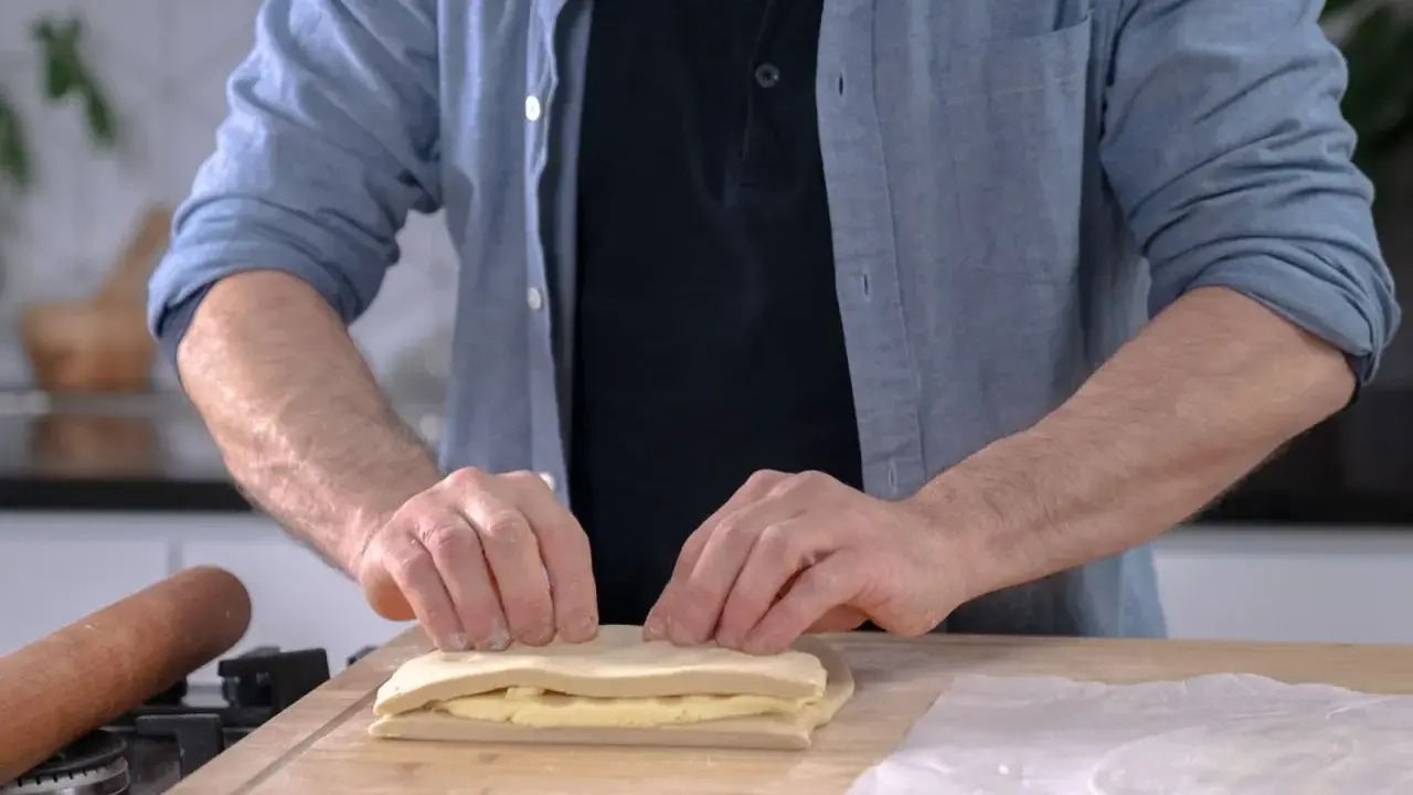 Un homme plie une pâte feuilletée professionnelle sur une planche en bois, prêt à créer des couches parfaites.