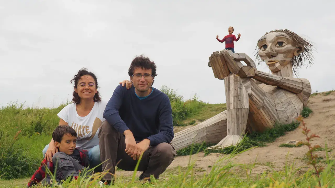 Familia disfrutando de Copenhague con niños, posando ante una escultura gigante de madera. Un niño pequeño juega en la mano de la figura.
