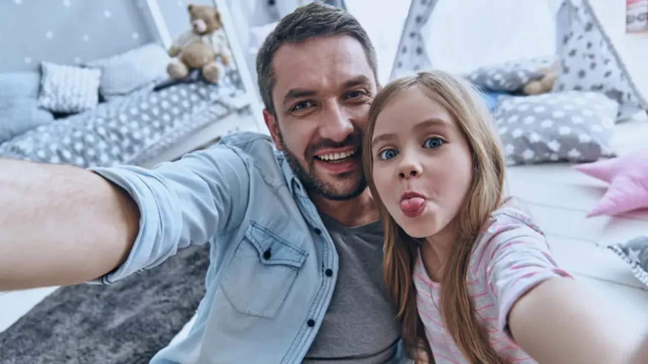 Padre e figlia si scattano un selfie giocoso, un'immagine che cattura la gioia del loro rapporto padre-figlia, quasi come in un'interpretazione freudiana della felicità.