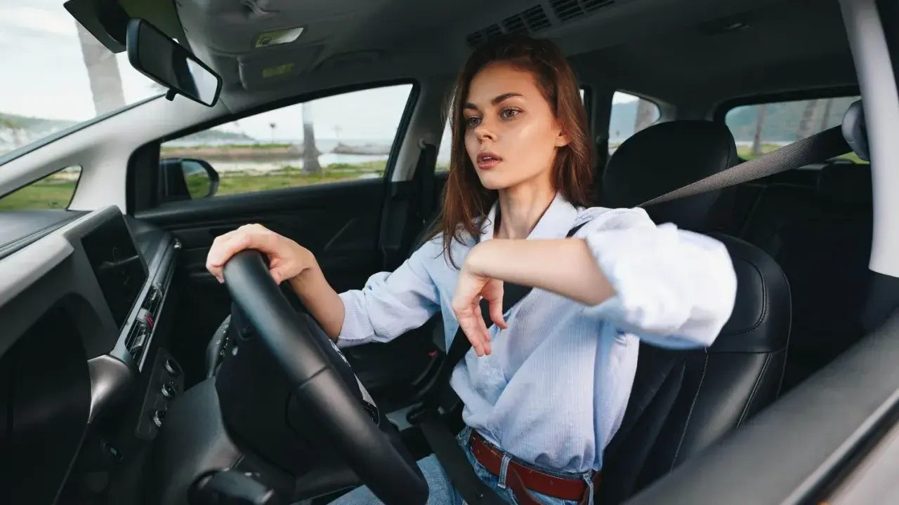 Kobieta za kierownicą zastanawia się, czy OC przedłuża się automatycznie. Widok na morze i palmy.