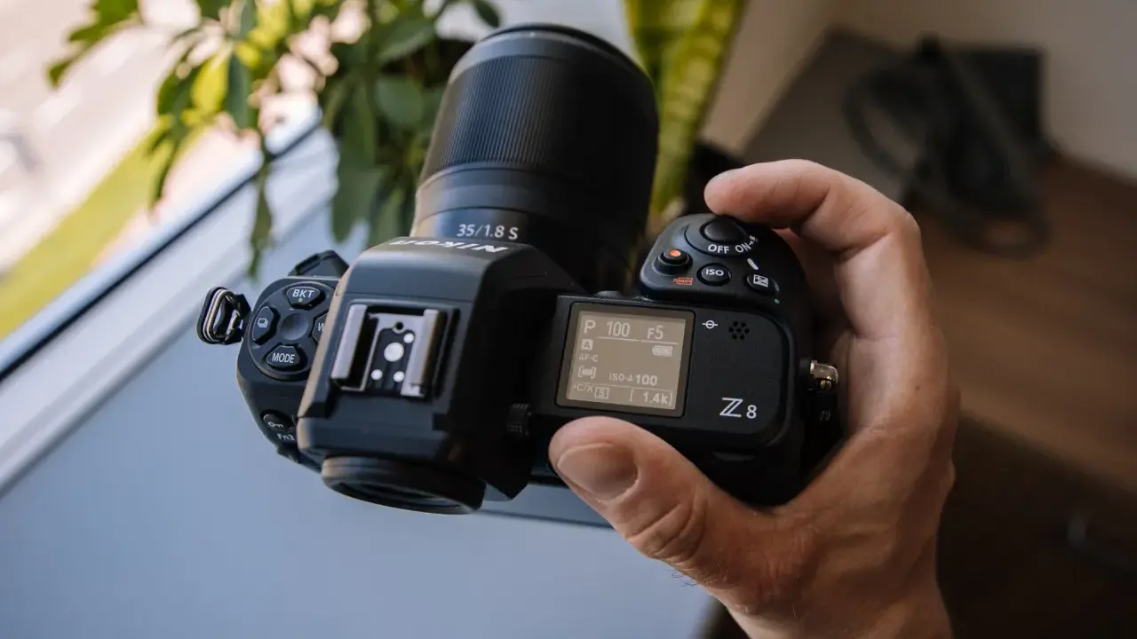 Dłoń trzyma aparat Nikon Z8 z obiektywem 35/1.8 S. Ekran pokazuje ustawienia, a cena tego modelu jest atrakcyjna.