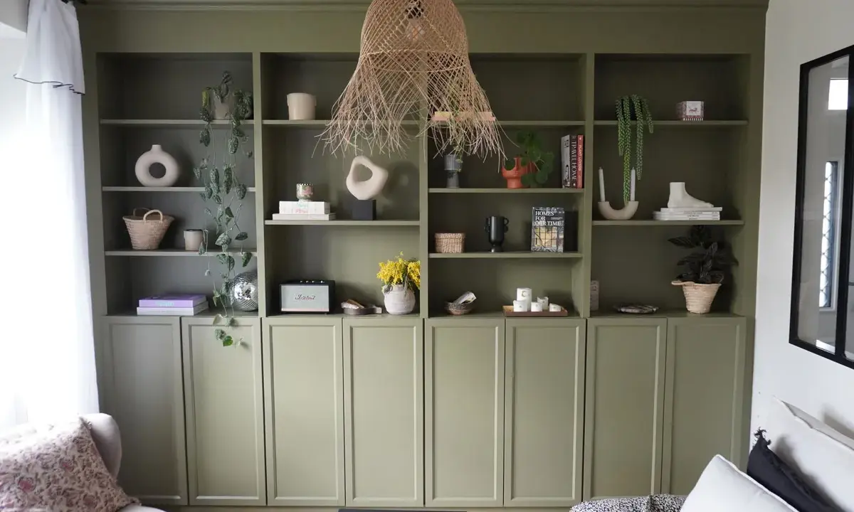 Une belle idée de bibliothèque salon avec des étagères vertes remplies de vases, plantes, livres et objets déco.
