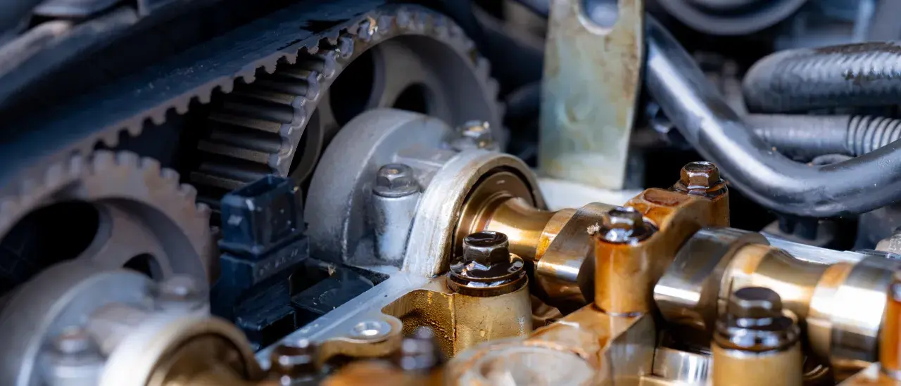 Zbliżenie na mechanizm rozrządu silnika, widoczny pasek zębaty i wałek rozrządu. Luźny pasek rozrządu objawy mogą być groźne dla silnika.