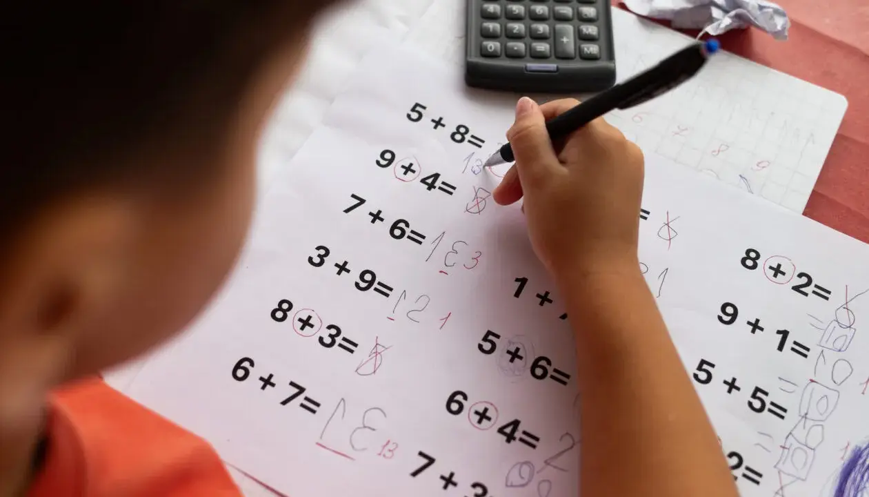 Dziecko zmagające się z zadaniami matematycznymi, być może z dyskalkulią. Widoczne są próby rozwiązywania przykładów i kalkulator.