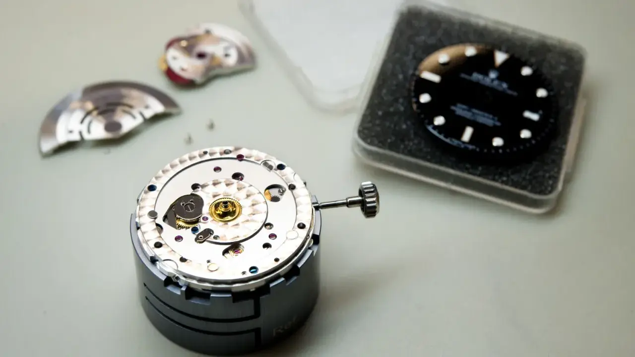 Parti di un movimento di orologio di lusso, tra cui il quadrante nero e la corona, pronti per l'assemblaggio.