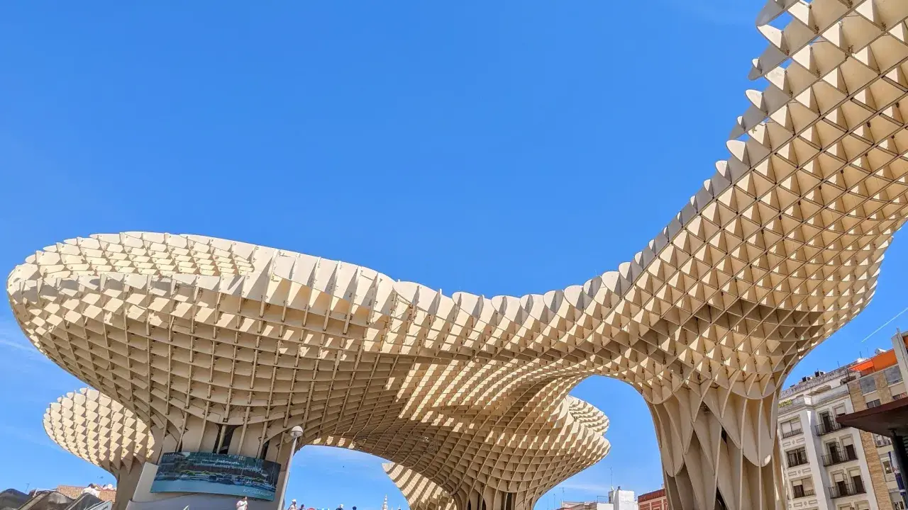 Der Metropol Parasol in Sevilla ragt mit seiner Holzkonstruktion in den blauen Himmel. Menschen steigen die Treppen hinauf.