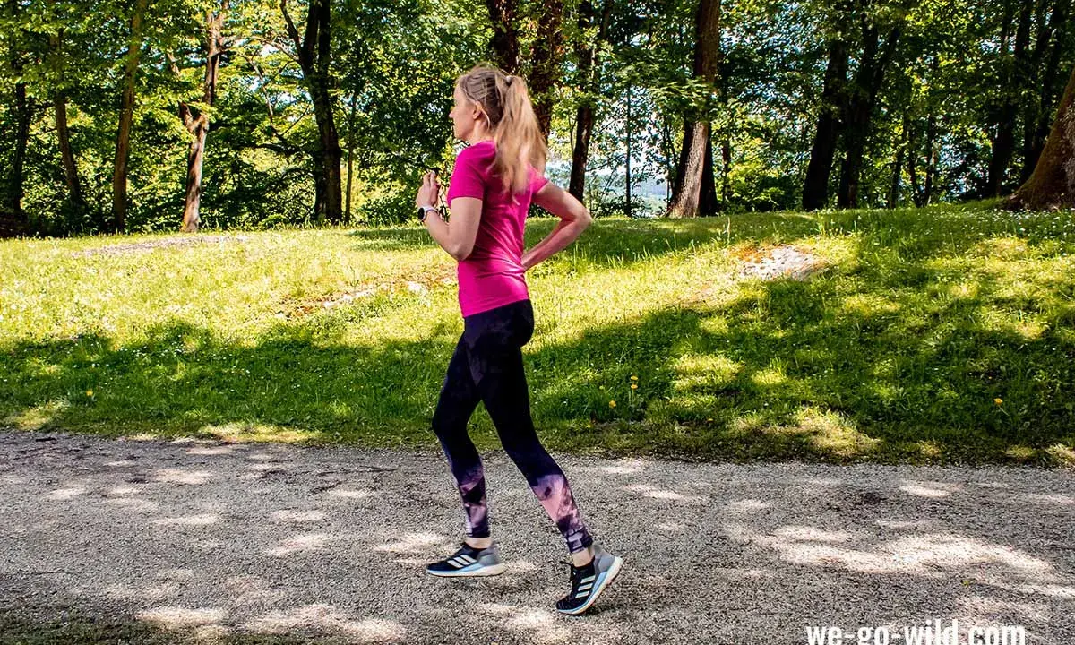 Frau läuft im Wald, um sich aufzuwärmen. Sonnenschein und grüne Bäume schaffen eine idyllische Kulisse für ihr Training.