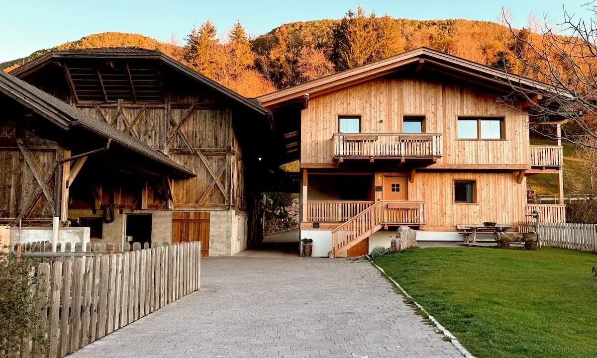 Maso Gallo Rosso: un'accogliente casa in legno e un fienile rustico immersi nel paesaggio alpino al tramonto.