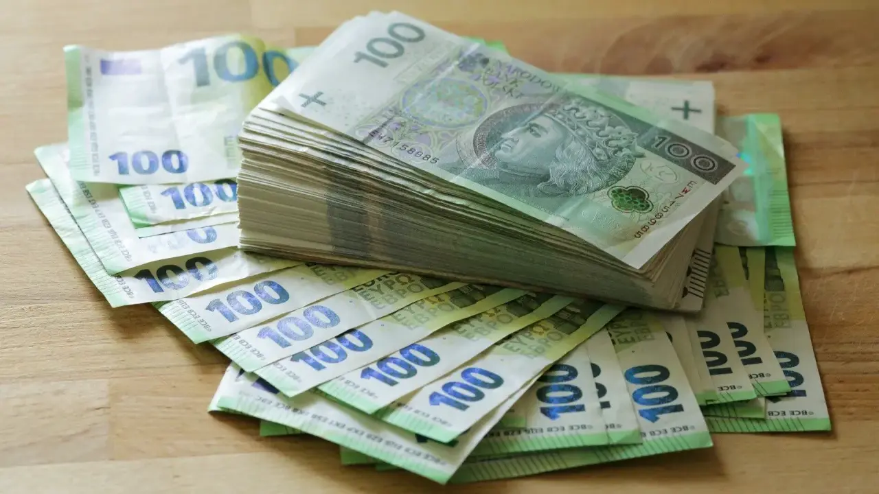 Stos banknotów 100 zł i 100 euro na drewnianym blacie. Może to być kwota na zasiłek stały.