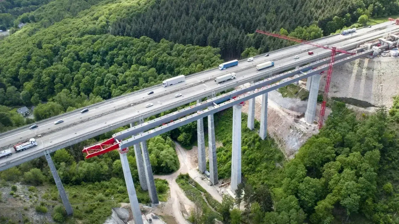 Wysoki wiadukt z betonowymi filarami, na którym widać ruch samochodowy. Konstrukcja z betonu C30/37 wznosi się nad zielonym lasem.