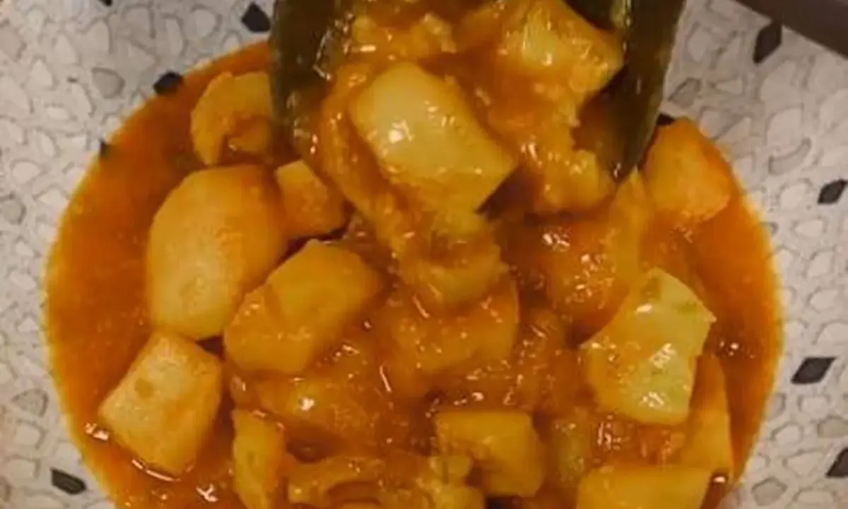Un plato de papas con choco en una salsa naranja, servido en un cuenco con un patrón de puntos.