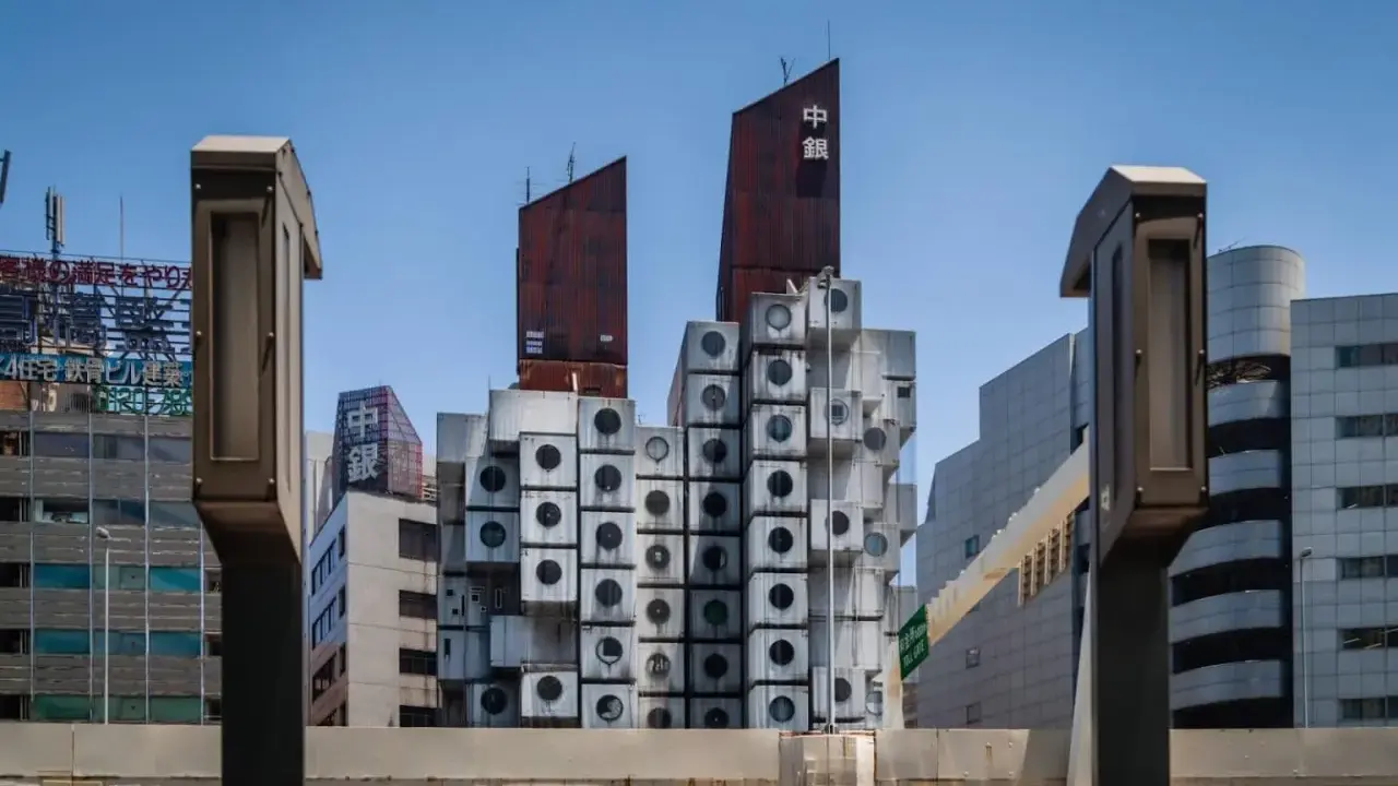 Iconica Nakagin Capsule Tower, un capolavoro di architettura modulare con capsule cubiche impilate, si staglia contro il cielo azzurro.