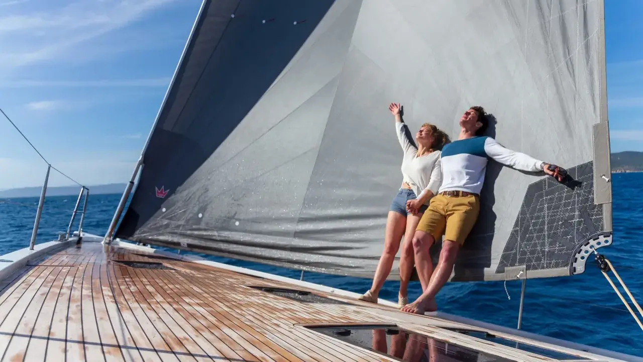Un couple heureux profite du soleil sur un voilier. Ils semblent avoir fait le bon choix en décidant de choisir un voilier pour leurs vacances.