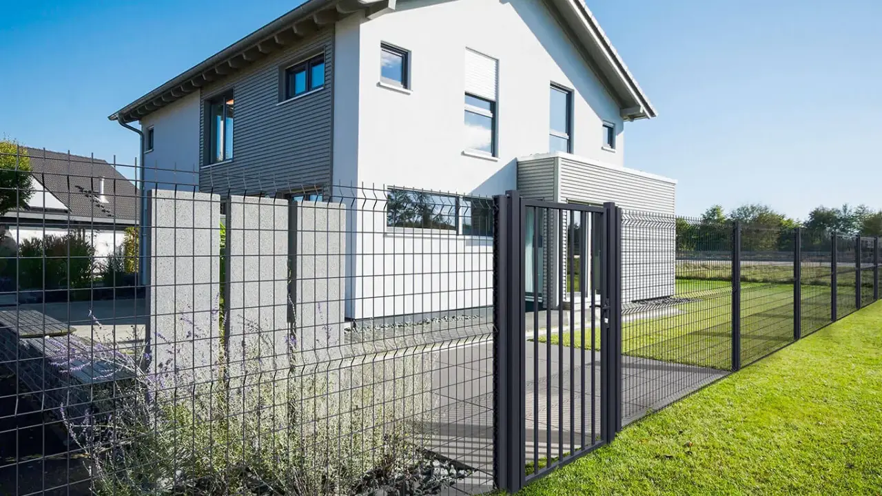 Maison moderne avec portail et pose grillage rigide, délimitant un jardin verdoyant.