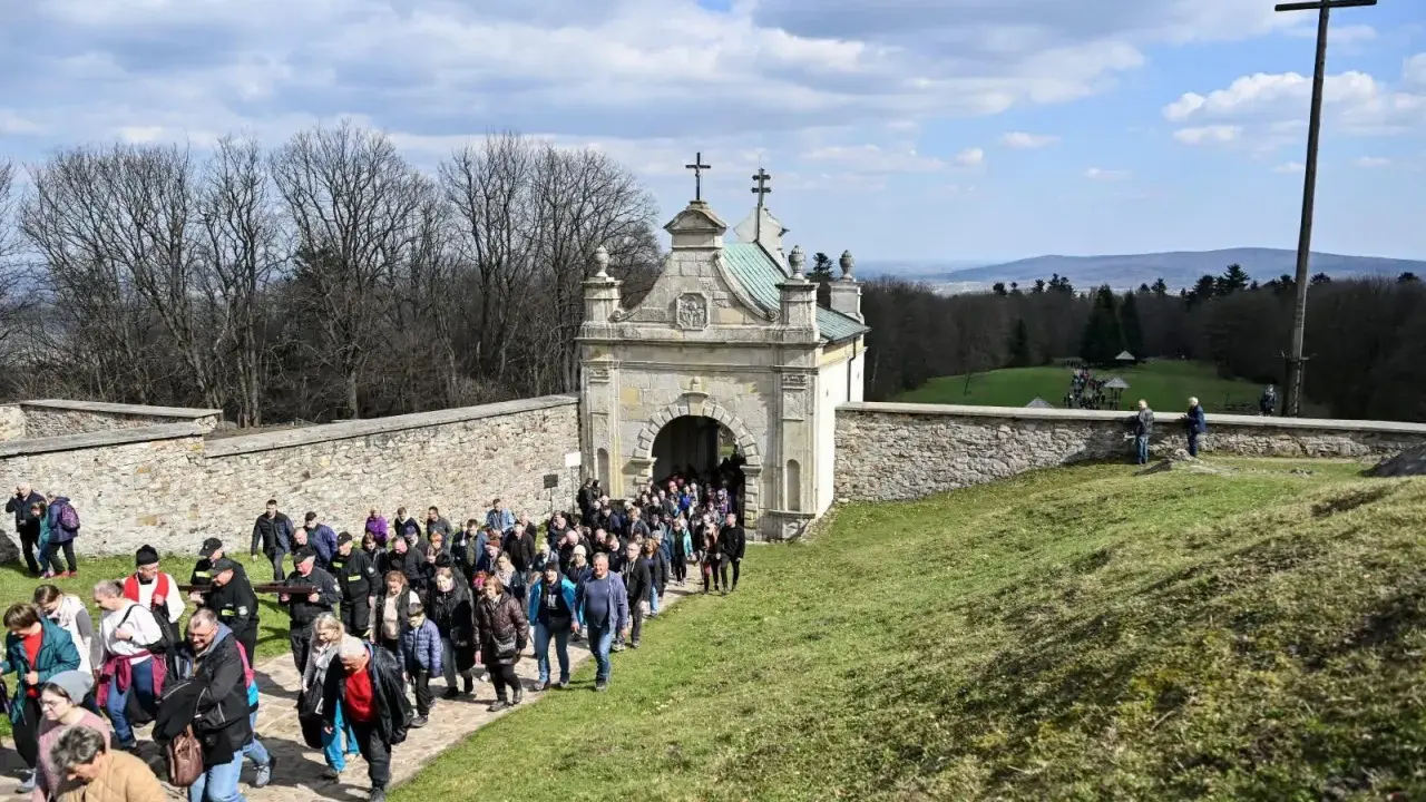 Pielgrzymka wchodzi przez zabytkową bramę. W oddali widać krzyż i piękne krajobrazy, które są nowa słupia atrakcje.