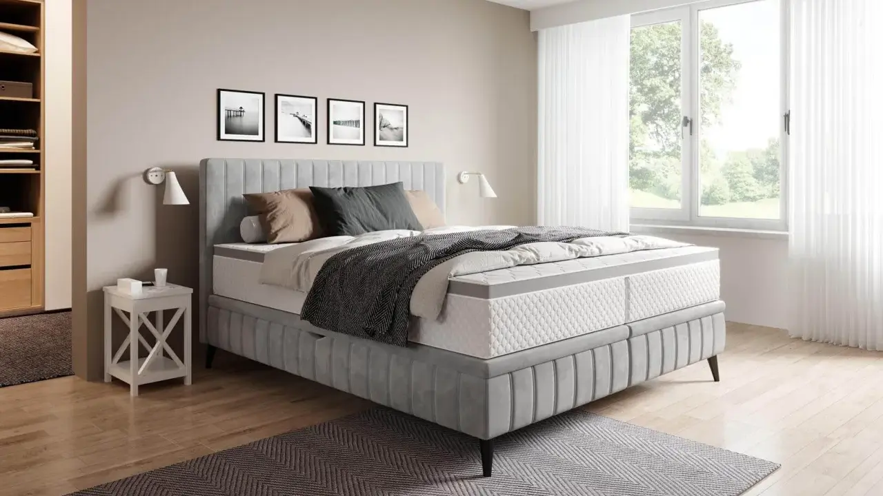 Sovrum med en stor säng i grått tyg. En fin balans att blanda beige och grått inredning med detaljer i trä och svarta tavlor på väggen.