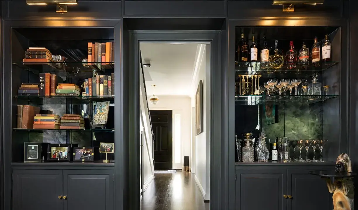 Estanterías oscuras con libros, botellas y copas. Ideas para como decorar una libreria con estilo y elegancia.
