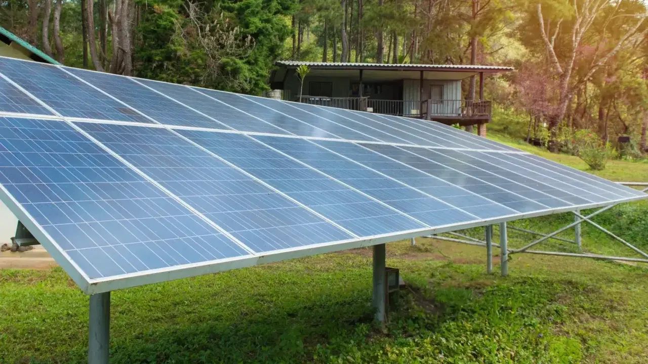 Grandes panneaux solaires au sol, installés dans un jardin verdoyant, captent l'énergie du soleil pour alimenter une maisonnette en bois.