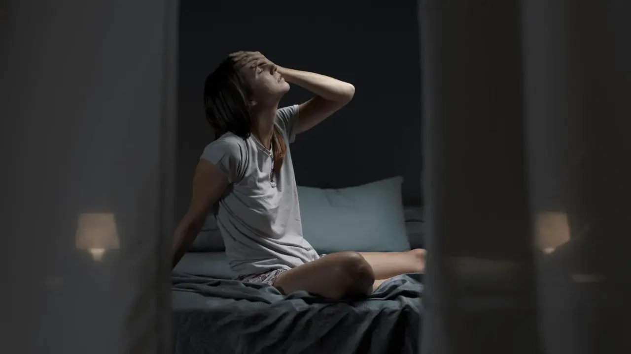 Donna seduta a letto, con la mano sulla fronte, soffre di sudore notturno al collo.