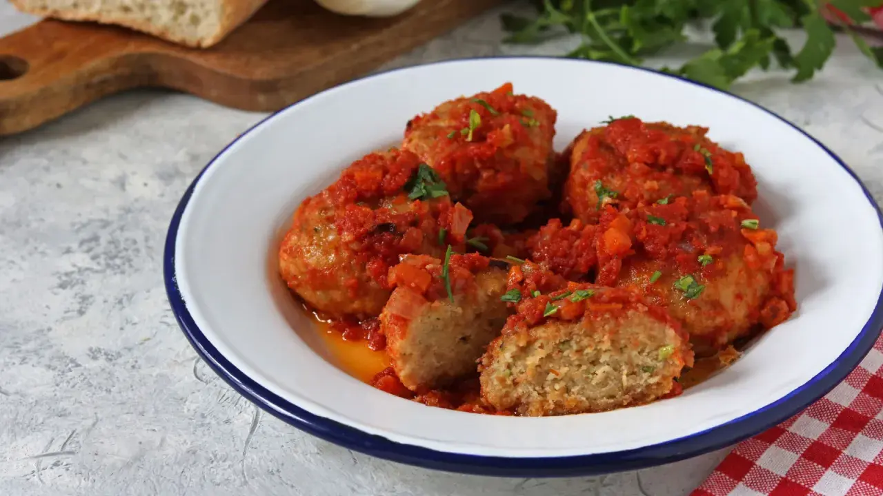 Polpette di pane succulente in salsa di pomodoro, guarnite con prezzemolo fresco. Un piatto casalingo che profuma di tradizione.