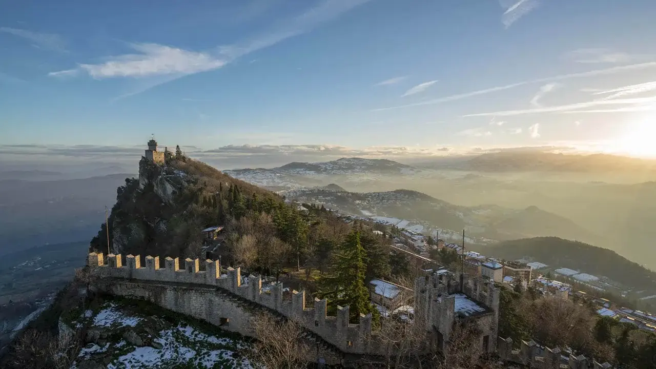Un suggestivo viaggio a San Marino: torri medievali su un crinale roccioso, con la nebbia che avvolge le valli sottostanti al tramonto.