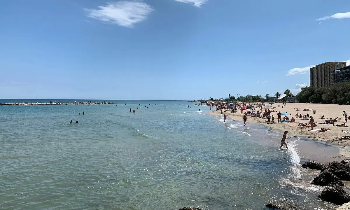 Sonniger bari strand mit vielen Menschen, die im Meer schwimmen und sich am Sand sonnen.