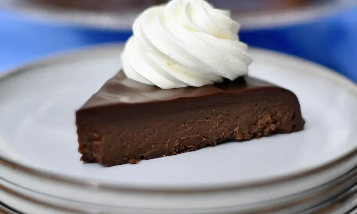 En bit fransk chokladtårta med en virvel av vispad grädde på en tallrik.