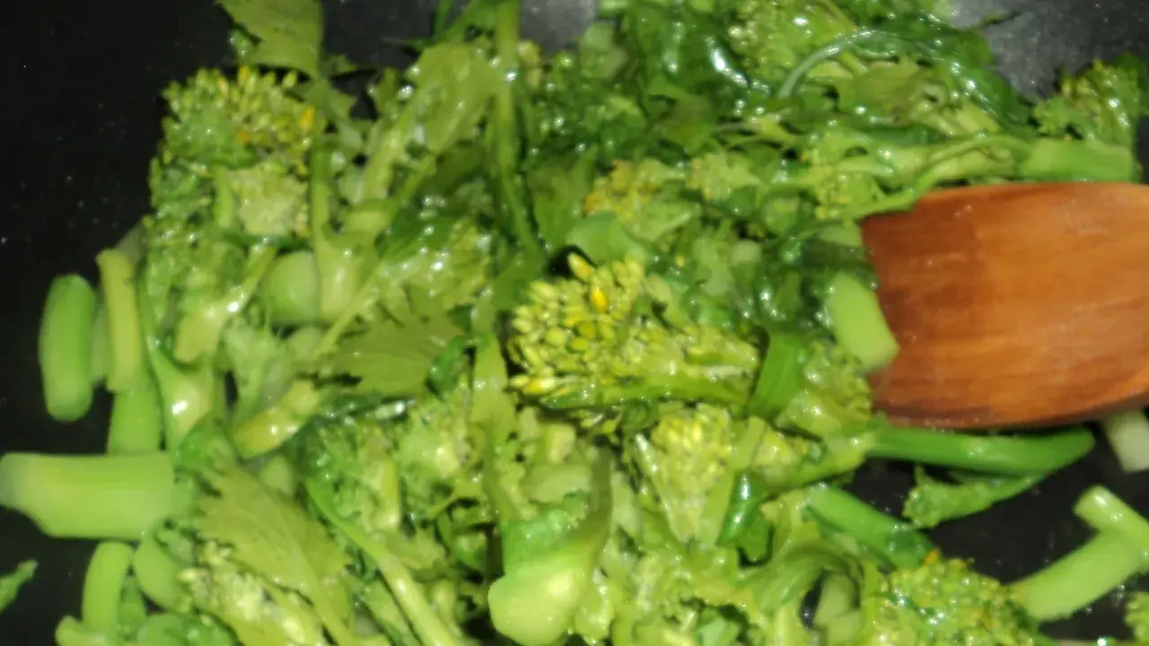 Cime di rapa salteados en sartén con una cuchara de madera. Verduras verdes vibrantes y frescas, listas para ser disfrutadas.