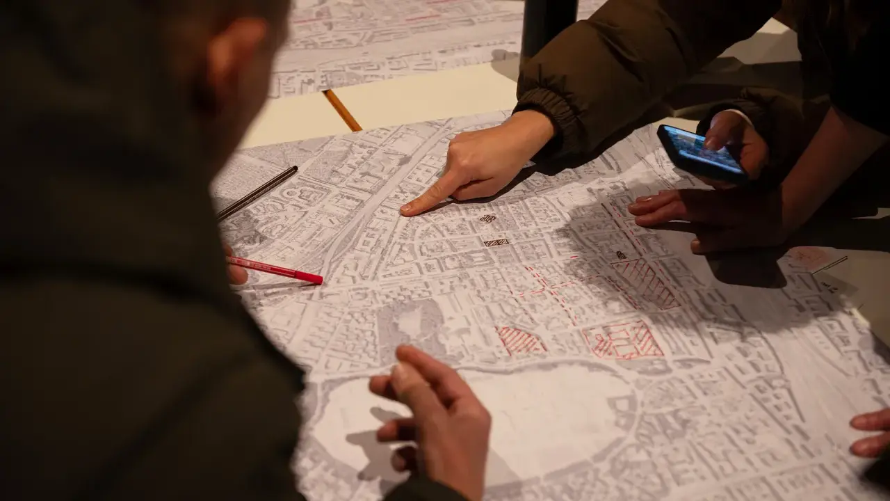 Menschen diskutieren auf einer Karte, die Details der Stadt zeigt. Sie planen die monitoring soziale stadtentwicklung, markieren Bereiche und nutzen ein Smartphone.