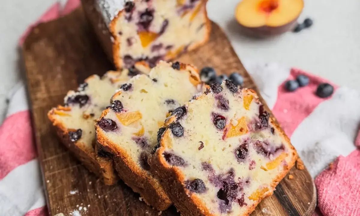 Saftiger Joghurt Kuchen mit Blaubeeren und Pfirsichstücken, bestäubt mit Puderzucker.