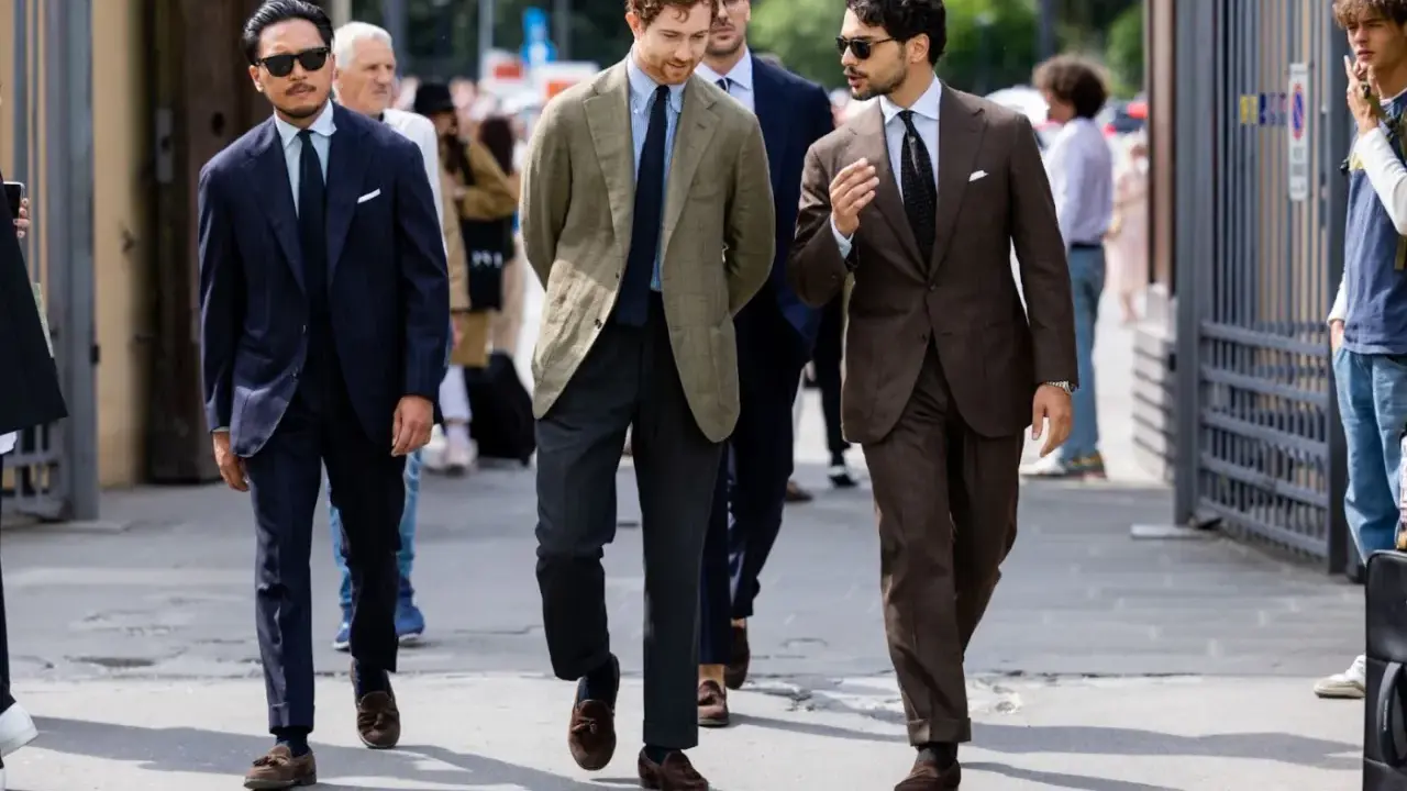 Trzech mężczyzn w eleganckich garniturach i stylowych loafersach do garnituru idzie ulicą.