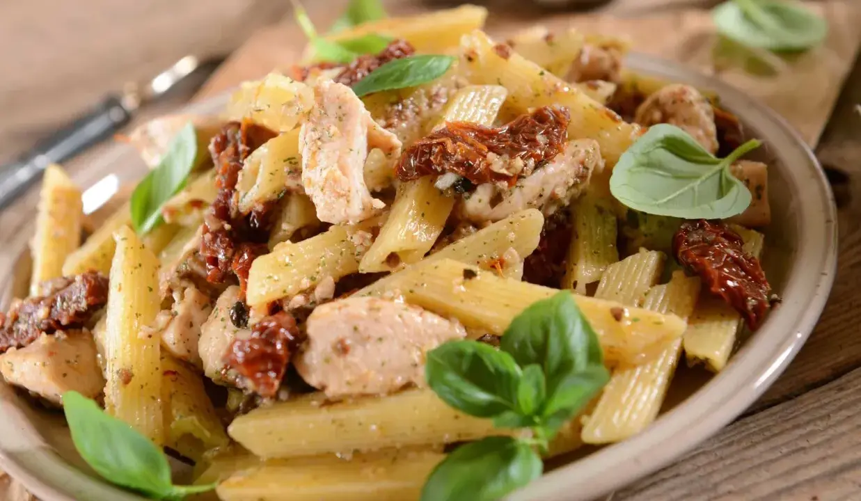 Penne z kurczakiem i suszonymi pomidorami, ozdobione świeżą bazylią. Pyszne danie, które zachwyci każdego smakosza.