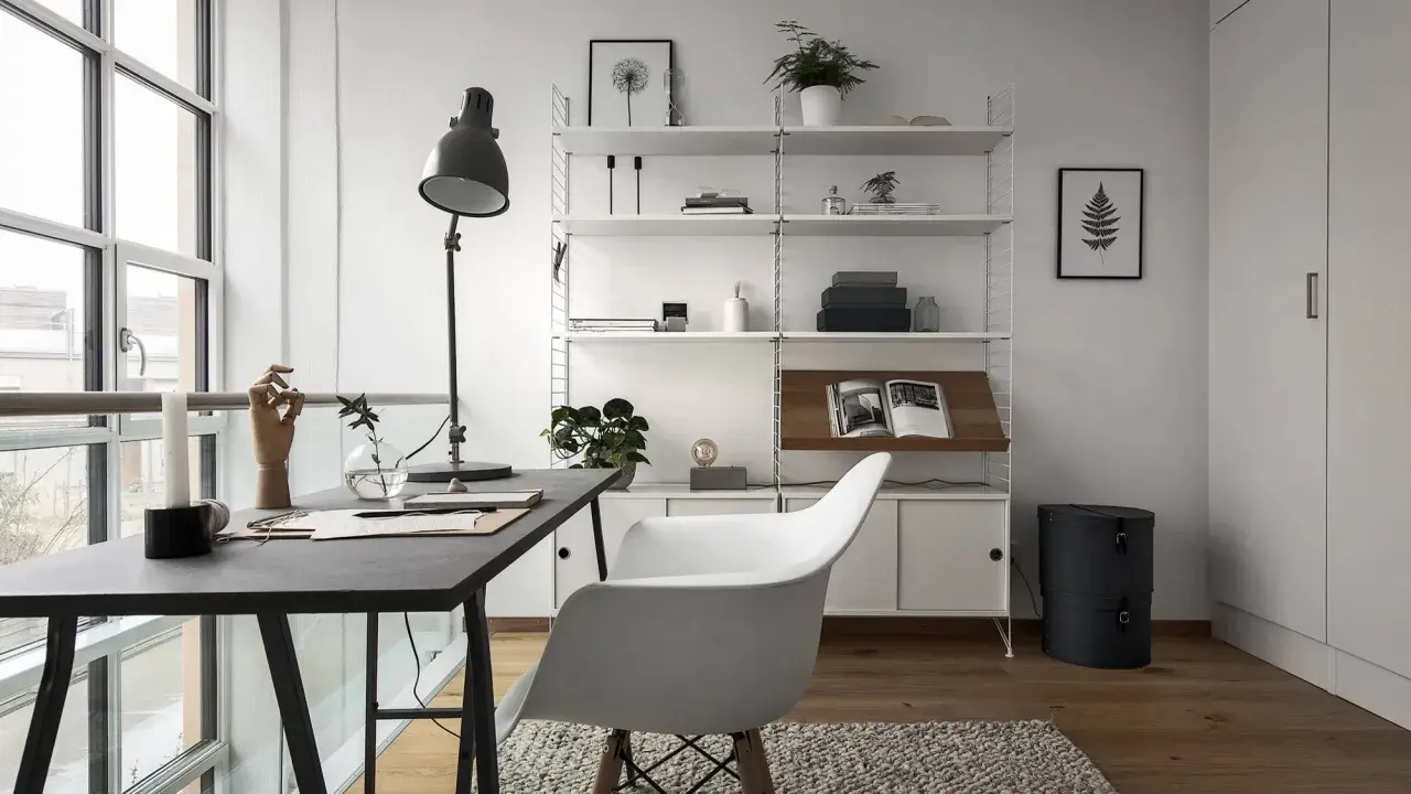 Ett modernt hemmakontor med ett mörkt skrivbord, en vit stol och en stilren, inredd bokhylla. Ljuset flödar in från stora fönster.