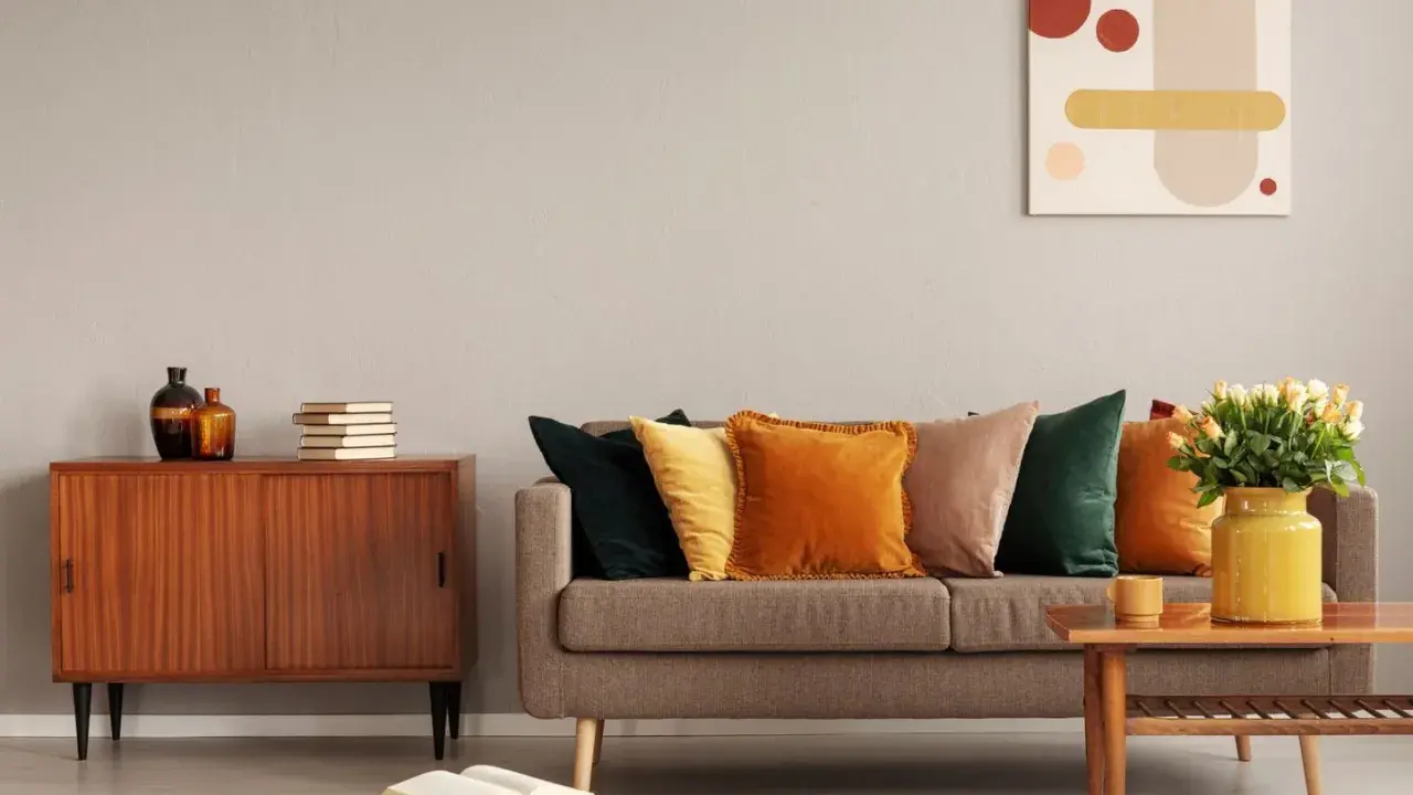 Un salon cosy aux couleurs automnales, avec un canapé garni de coussins ocre et vert forêt, un meuble vintage en bois et une peinture abstraite.