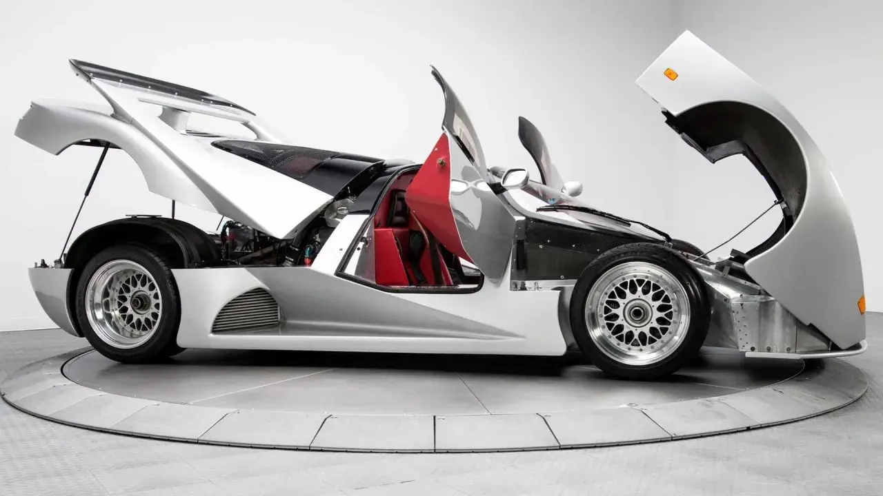 Silberner Lotec C1000 Supersportwagen mit geöffneten Türen und Hauben, rote Sitze und sichtbarer Motor.