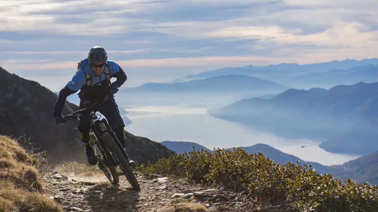 Ein Mountainbiker auf einer abenteuerlichen Tour in den Alpen, mit einem See und Bergketten im Hintergrund.