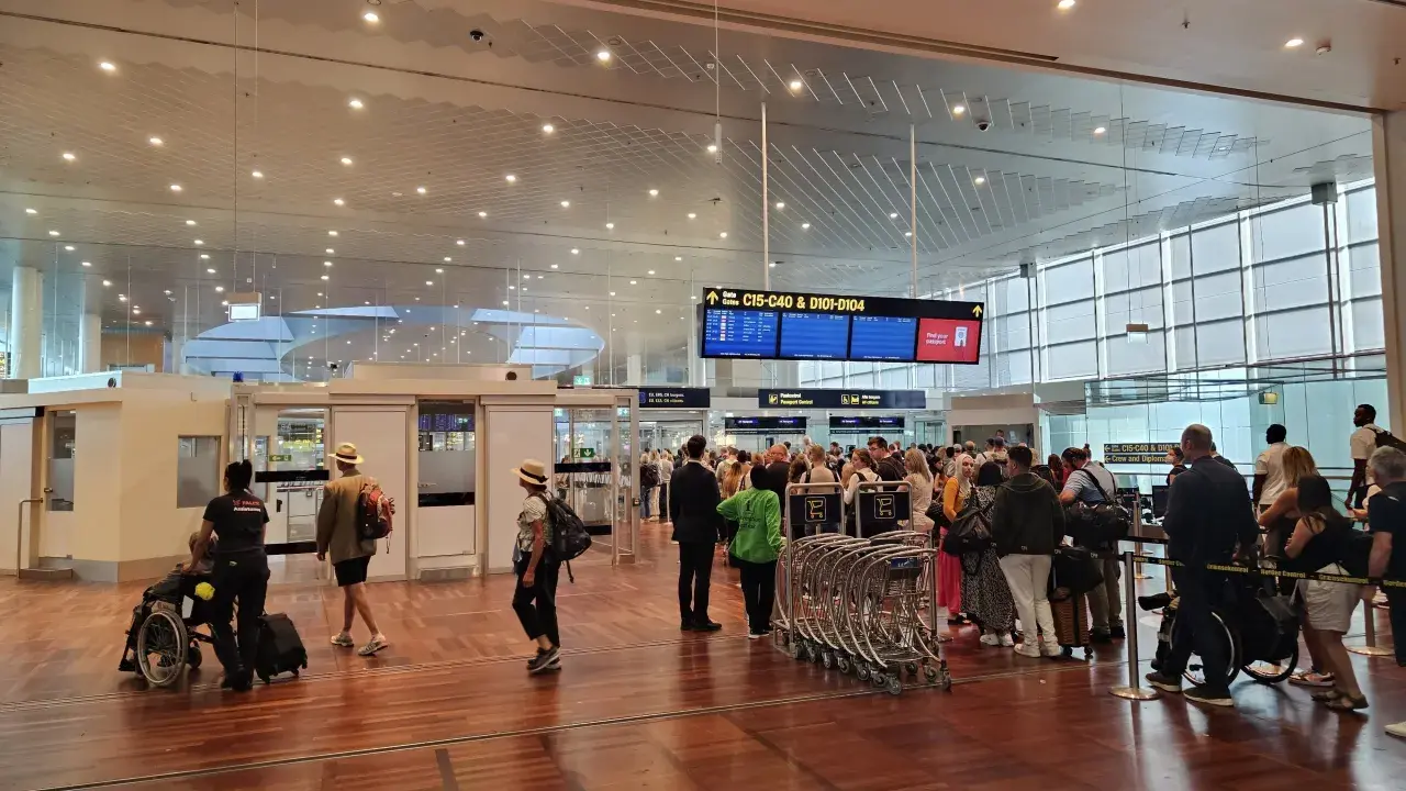 Ludzie w terminalu lotniska, tablice z informacjami o bramkach i pasażerowie z bagażami.