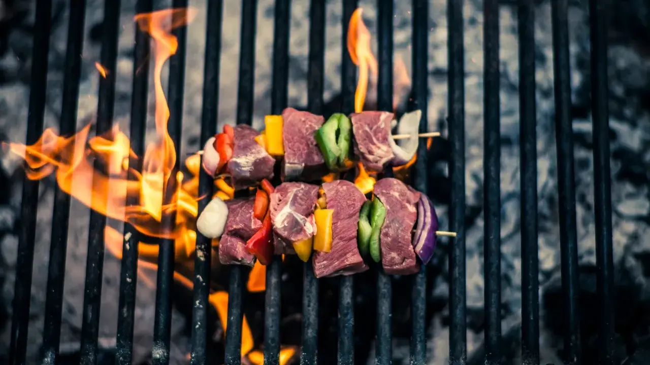 Brochetas de carne y verduras sobre parrilla de carbón, llamas naranjas. ¡Así se hace barbacoa carbón!
