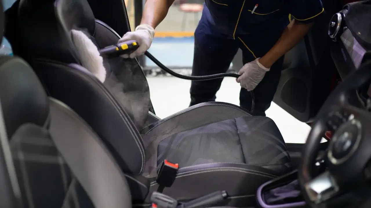 Un profesional usa vapor para limpiar los asientos del coche, mostrando cómo limpiar los asientos del coche de forma efectiva.